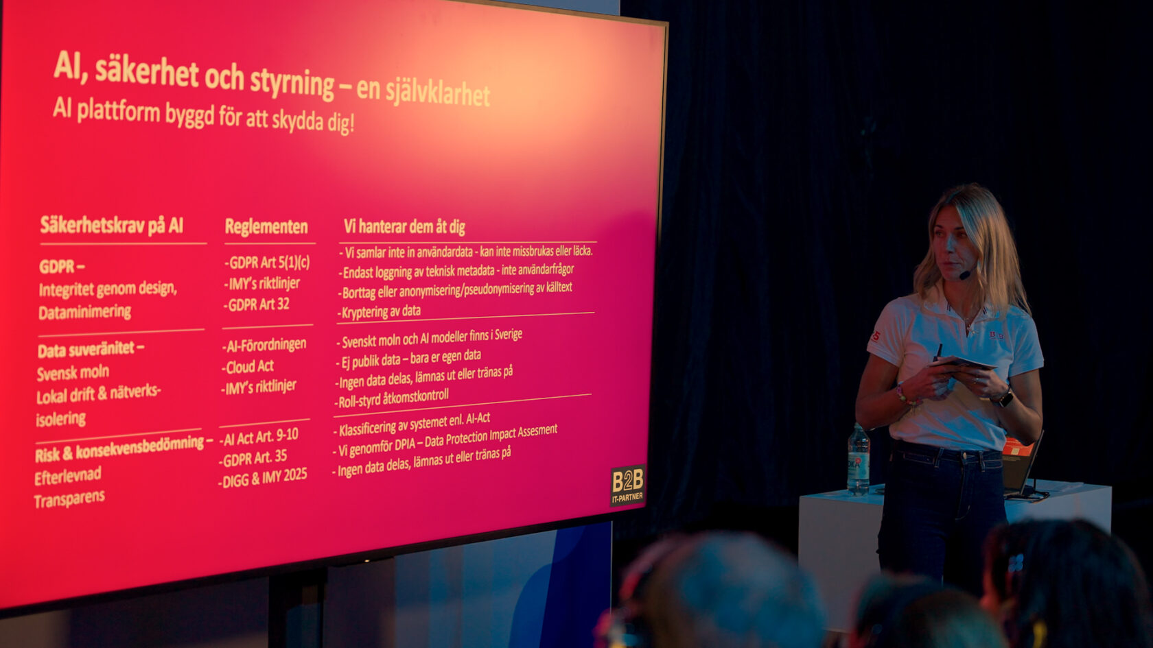 Kvinna står bredvid en stor skärm med presentation om AI, säkerhet och styrning, riktad till en publik.