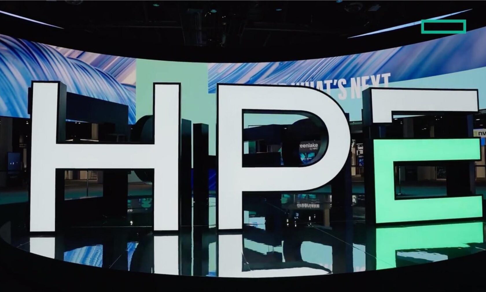 Stora, upplysta bokstäver som stavar "HPE" på en mässa med digital skärm i bakgrunden.
